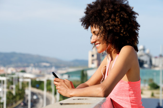 side-portrait-of-young-woman-with-headphones-outside-holding-mobile-phone_33839-9953